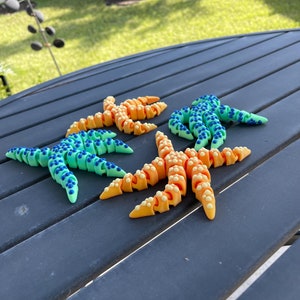 May include: Three colorful starfish made of plastic, with blue, green, and orange colors. The starfish are on a black table.