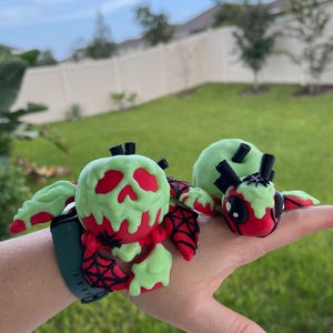Puede incluir: Accesorio decorativo verde y rojo para smartwatch. Presenta un dise&ntilde;o de calavera con un efecto verde goteante, detalles rojos y una telara&ntilde;a. La correa del reloj es verde oscuro.