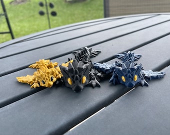 May include: Three small dragon figurines, one gold, one black, and one blue, with yellow eyes. The dragons are posed in a crawling position with their wings spread out.