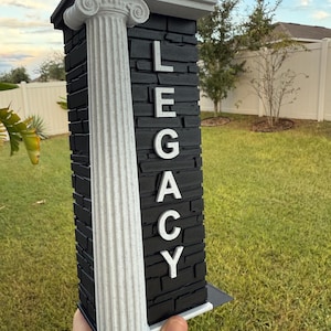 May include: A decorative pillar with the word "LEGACY" in white letters. The pillar has a black stone-like texture and a white column on the left side. The top and base are also white.