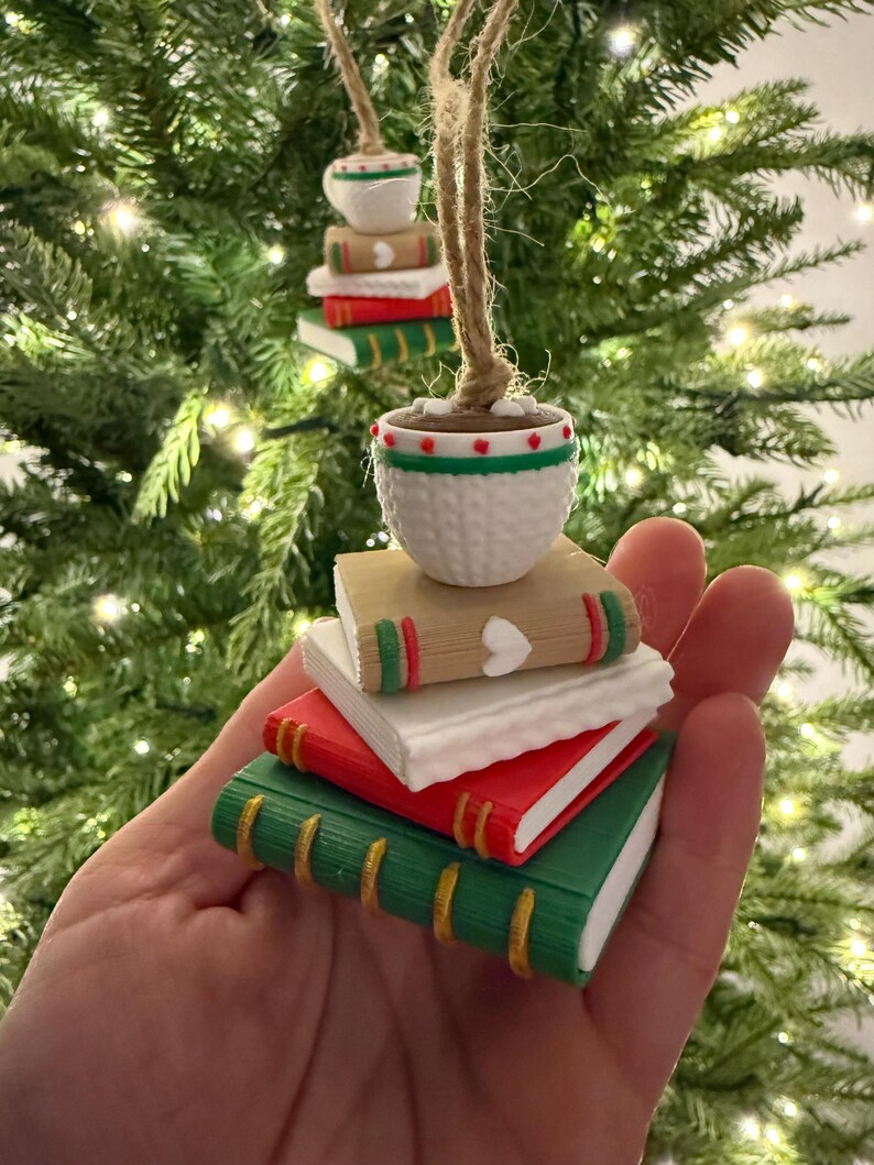 K&ouml;nnte beinhalten: Miniatur-Buchornamente mit einem kleinen Topf obenauf, an Schnur aufgeh&auml;ngt. Die B&uuml;cher sind rot, wei&szlig; und gr&uuml;n mit goldenen Akzenten. Der Topf ist wei&szlig; mit roten und gr&uuml;nen Details. Auf einem Weihnachtsbaum ausgestellt.