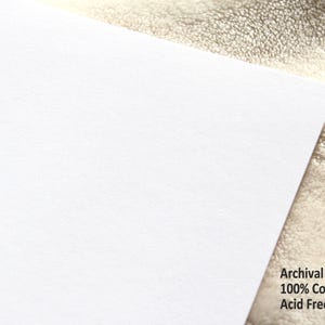 May include: A corner of a bright white paper sheet with the text "Archival Grade 100% Cotton Acid Free" in black. The paper has a slightly textured surface and is set against a neutral background.