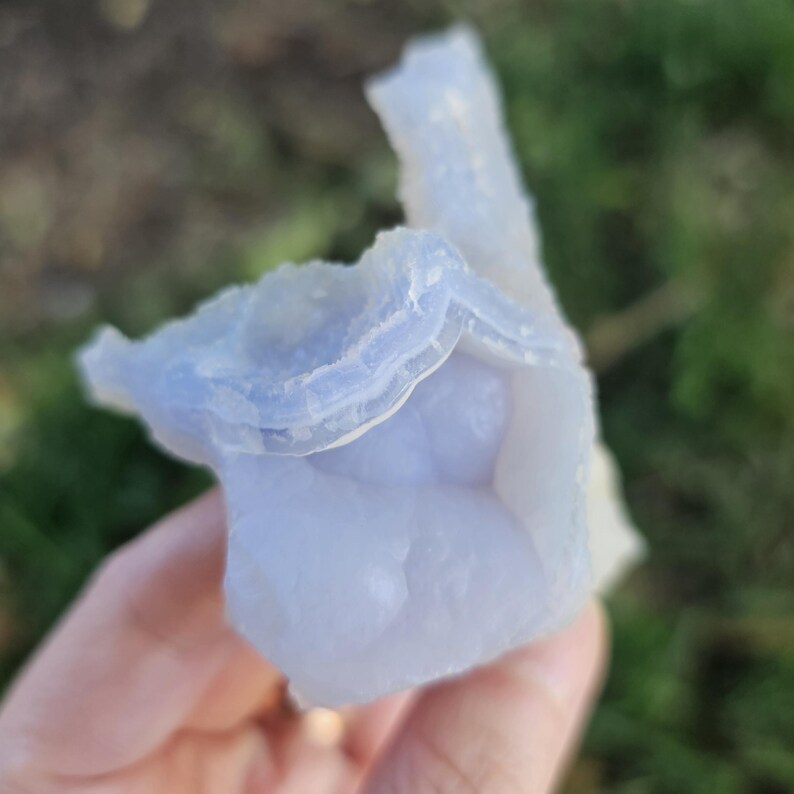 Close-up view of the raw African Blue Lace Agate cluster from an alternate angle, highlighting its complex, open-ended geometric shape, natural etching, and how the light catches the delicate blue and white bands.