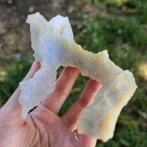 Close-up view of the raw African Blue Lace Agate cluster from an alternate angle, highlighting its complex, open-ended geometric shape, natural etching, and how the light catches the delicate blue and white bands.