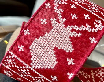 May include: Close-up of a red ribbon with a white knitted pattern featuring a Christmas tree design. The ribbon has a textured surface and is likely used for holiday decorations or gift wrapping. The ribbon is rolled up.