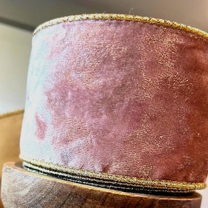 May include: A roll of dusty rose velvet ribbon with a gold trim. The ribbon is sitting on a wooden spool. The ribbon has a soft, textured appearance and is suitable for crafts and decorations.