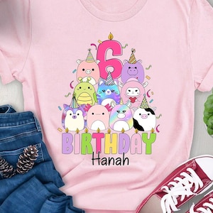Puede incluir: Camiseta rosa con un gráfico de un pastel de cumpleaños con una vela número 6 y lindos personajes de animales. El texto "BIRTHDAY Hannah" está debajo del pastel.