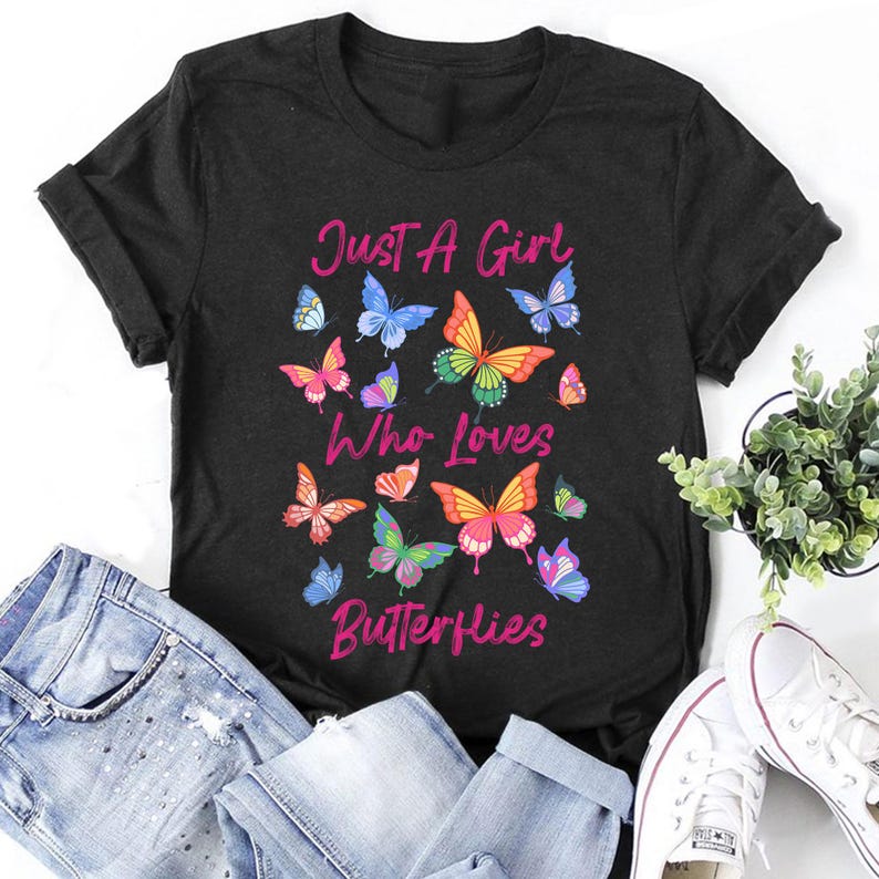 May include: Black t-shirt with the text "Just a Girl Who Loves Butterflies" in pink lettering. The shirt is decorated with colorful butterfly illustrations.