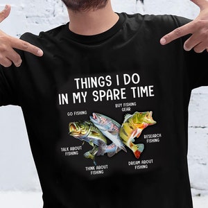 May include: A black t-shirt with white text that reads "Things I do in my spare time."  The text is surrounded by illustrations of fish, including a bass, a trout, and a perch.  The text below the fish reads "Go fishing", "Buy fishing gear", "Talk about fishing", "Research fishing", "Think about fishing", and "Dream about fishing."