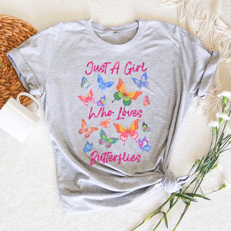 May include: Gray t-shirt with the text "Just a Girl Who Loves Butterflies" in pink lettering. The shirt is decorated with colorful butterfly illustrations.