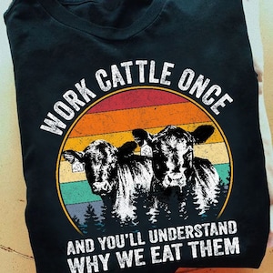 May include: Black t-shirt featuring a vintage-style graphic of two cows in front of a sunset. The text "Work Cattle Once And You'll Understand Why We Eat Them" is printed on the shirt.
