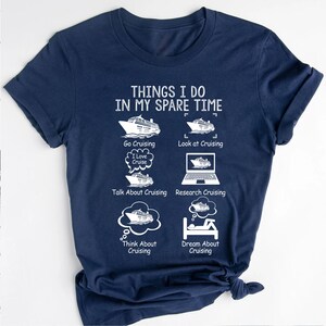 May include: A navy blue t-shirt with white text that reads "Things I do in my spare time". The text is followed by a list of activities related to cruising, including "Go Cruising", "Look at Cruising", "Talk About Cruising", "Research Cruising", "Think About Cruising", and "Dream About Cruising". Each activity is illustrated with a simple drawing of a cruise ship.