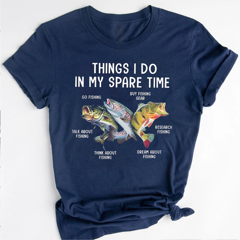 May include: A navy blue t-shirt with the text "THINGS I DO IN MY SPARE TIME" and a graphic of fish with text describing different fishing activities. The text includes: "GO FISHING", "BUY FISHING GEAR", "TALK ABOUT FISHING", "RESEARCH FISHING", "THINK ABOUT FISHING", and "DREAM ABOUT FISHING".