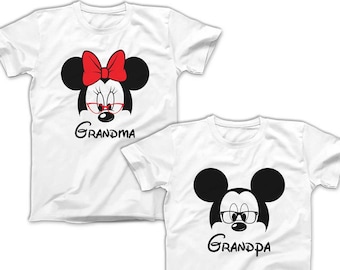 May include: Two white t-shirts with a cartoon image of Mickey Mouse and Minnie Mouse wearing glasses. The Minnie Mouse shirt says "Grandma" and the Mickey Mouse shirt says "Grandpa".