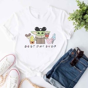 May include: White t-shirt with a green cartoon character wearing Mickey Mouse ears and holding a Mickey Mouse ice cream cone. The text "BEST DAY EVER" is printed below the character.
