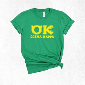 May include: A green t-shirt with the text "OK Oozma Kappa" in yellow. The shirt has rolled-up sleeves and is knotted at the bottom. The shirt is made of a soft material.