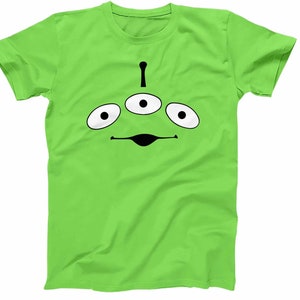 May include: A green t-shirt with a black alien face design. The alien has three eyes and a small mouth.