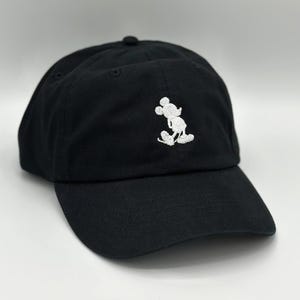 May include: Black baseball cap with a curved brim. The cap features a white embroidered image of Mickey Mouse on the front. The cap is made of a soft fabric and has a rounded crown.
