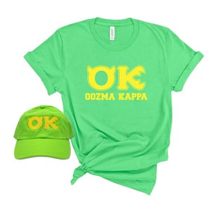 May include: A lime green t-shirt and baseball cap set. The t-shirt features the text "OK Oozma Kappa" in yellow. The baseball cap has the same "OK" logo embroidered in yellow. Both items are displayed on a white background.