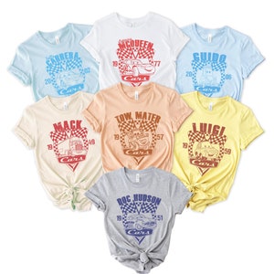 以下が含まれることがあります： 映画「カーズ」をテーマにした、異なるキャラクターが描かれた6枚のTシャツのセット。Tシャツは、薄い青、白、桃色、ベージュ、黄色、グレーなど、さまざまな色があります。各Tシャツには、キャラクターの名前と番号が書かれた市松模様のデザインが施されています。