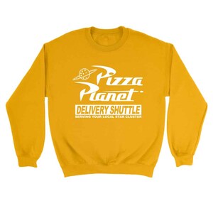 Pu&ograve; includere: Felpa gialla con una grafica bianca di un logo di Pizza Planet con il testo "Pizza Planet Delivery Shuttle Serving Your Local Star Cluster".