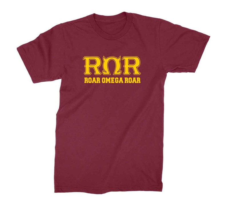 Peut inclure: Un t-shirt bordeaux avec un motif dor&eacute; qui dit "ROR" et "ROAR OMEGA ROAR".