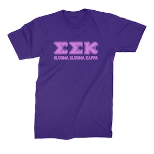 Peut inclure: T-shirt violet avec un motif de lettres grecques roses qui dit "&Sigma;&Sigma;&Kappa;" et "SLUGMA SLUGMA KAPPA" en lettres roses.