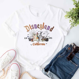 May include: White t-shirt with a purple, orange, and black graphic of the Nightmare Before Christmas characters in front of a Disneyland sign that reads "Disneyland Est. 1955 California".
