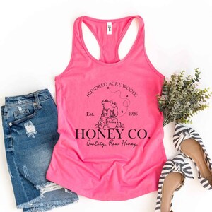 May include: Pink tank top with a black graphic of Winnie the Pooh and a honey pot. The graphic says "Hundred Acre Woods Est. 1926 Honey Co. Quality Raw Honey".