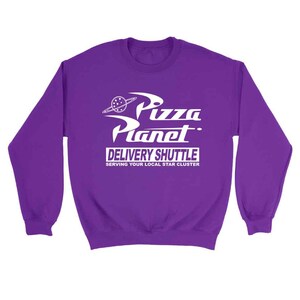 Pu&ograve; includere: Felpa viola con una grafica bianca del logo Pizza Planet, un ristorante a tema spaziale del film Toy Story. Il testo recita "Pizza Planet Delivery Shuttle Serving Your Local Star Cluster."