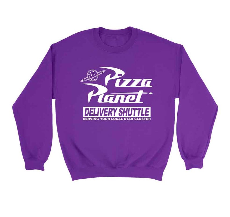 Pu&ograve; includere: Felpa viola con una grafica bianca del logo Pizza Planet, un ristorante a tema spaziale del film Toy Story. Il testo recita "Pizza Planet Delivery Shuttle Serving Your Local Star Cluster."