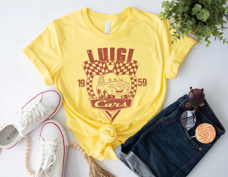 以下が含まれることがあります： 映画「カーズ」のルイージのヴィンテージスタイルのグラフィックがプリントされた黄色のTシャツ。グラフィックにはルイージの車、チェッカーフラッグ、そして「ルイージカーズ」というテキストと数字の19と59が描かれています。