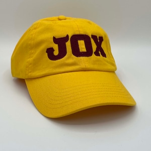 May include: A yellow baseball cap with a maroon embroidered "JOX" on the front.