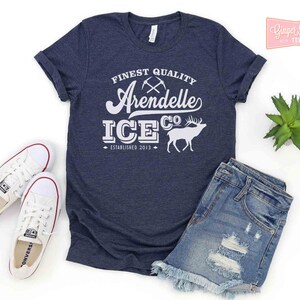 Puede incluir: Una camiseta azul marino con texto blanco que dice "FINEST QUALITY Arendelle ICE CO. ESTABLISHED 2013". El texto est&aacute; en una fuente de estilo vintage e incluye un gr&aacute;fico de dos picos cruzados y un ciervo.