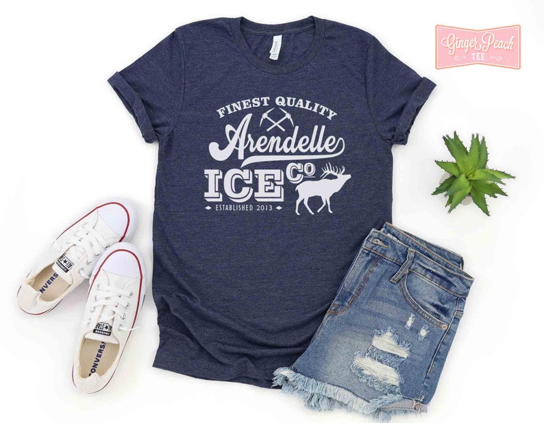 Puede incluir: Una camiseta azul marino con texto blanco que dice "FINEST QUALITY Arendelle ICE CO. ESTABLISHED 2013". El texto est&aacute; en una fuente de estilo vintage e incluye un gr&aacute;fico de dos picos cruzados y un ciervo.