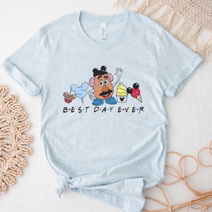 May include: Light blue t-shirt with a graphic of Mr. Potato Head and other Disney characters. The text "BEST DAY EVER" is printed below the graphic.