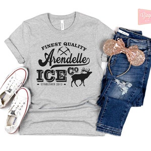 Puede incluir: Camiseta gris con texto negro que dice "Finest Quality Arendelle Ice Co. Established 2013". El texto est&aacute; en una fuente de estilo vintage. Hay dos picos cruzados sobre la palabra "Arendelle". Una silueta negra de un reno est&aacute; a la derecha del texto.