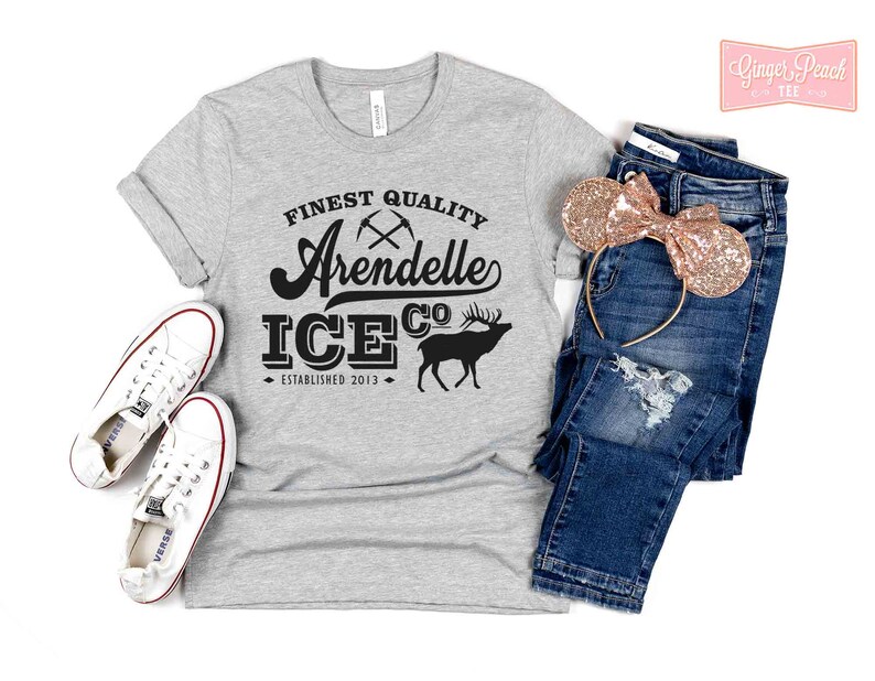 Puede incluir: Camiseta gris con texto negro que dice "Finest Quality Arendelle Ice Co. Established 2013". El texto est&aacute; en una fuente de estilo vintage. Hay dos picos cruzados sobre la palabra "Arendelle". Una silueta negra de un reno est&aacute; a la derecha del texto.