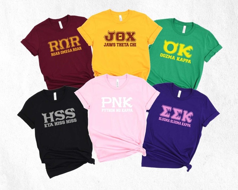 Peut inclure: Six t-shirts diff&eacute;rents avec des lettres grecques et des slogans. Les t-shirts sont de diff&eacute;rentes couleurs, notamment le marron, le jaune, le vert, le noir, le rose et le violet. Les slogans incluent "Roar Omega Roar", "Jaws Theta Chi", "Oozma Kappa", "Eta Hiss Hiss", "Python Nu Kappa" et "Slugma Slugma Kappa".