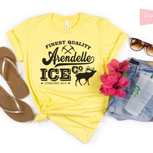 Puede incluir: Camiseta amarilla con un gr&aacute;fico negro que dice "Finest Quality Arendelle Ice Co. Established 2013" con un pico cruzado y un gr&aacute;fico de alce.