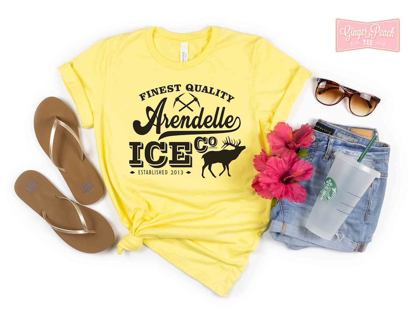 Puede incluir: Camiseta amarilla con un gr&aacute;fico negro que dice "Finest Quality Arendelle Ice Co. Established 2013" con un pico cruzado y un gr&aacute;fico de alce.