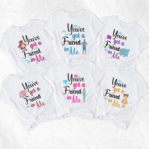 May include: Five white t-shirts with the phrase "You've got a Friend in Me" printed on them. Each shirt features a different character from the Toy Story franchise, including Woody, Buzz Lightyear, Rex, Hamm, and Bo Peep.