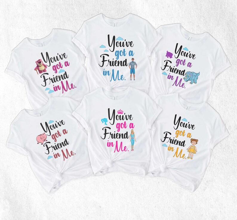 May include: Five white t-shirts with the phrase "You've got a Friend in Me" printed on them. Each shirt features a different character from the Toy Story franchise, including Woody, Buzz Lightyear, Rex, Hamm, and Bo Peep.