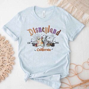 May include: Light blue t-shirt with a graphic print of the Disneyland logo and characters from the Nightmare Before Christmas. The text reads "Disneyland Est. 1955 California".