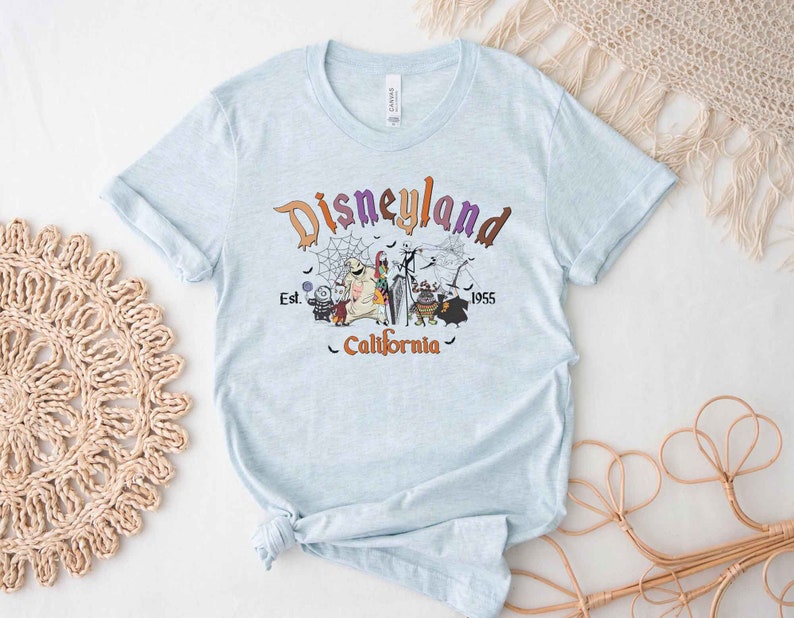 May include: Light blue t-shirt with a graphic print of the Disneyland logo and characters from the Nightmare Before Christmas. The text reads "Disneyland Est. 1955 California".