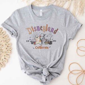 May include: A gray t-shirt with a graphic print of the Disneyland logo and characters from the Nightmare Before Christmas. The text reads "Disneyland Est. 1955 California".