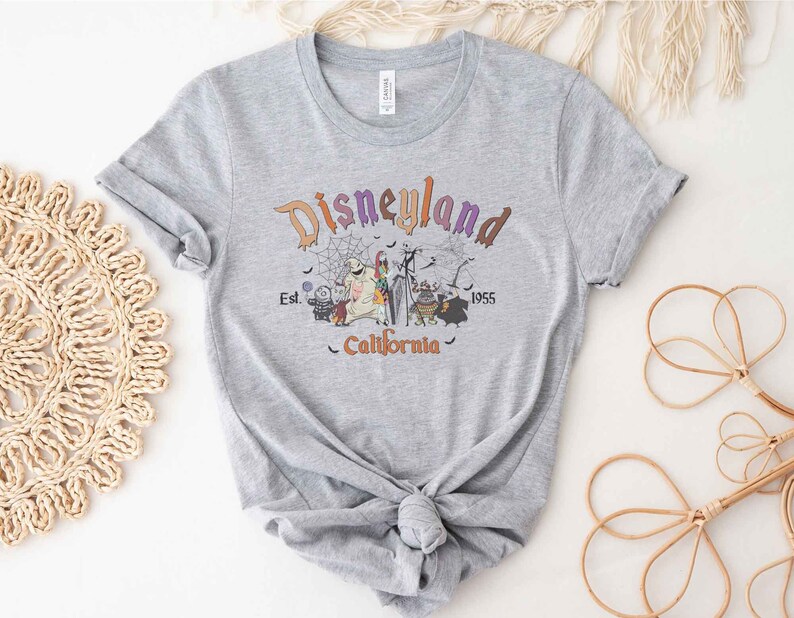May include: A gray t-shirt with a graphic print of the Disneyland logo and characters from the Nightmare Before Christmas. The text reads "Disneyland Est. 1955 California".
