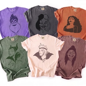 May include: Six short-sleeve crew neck t-shirts in various colors including purple, charcoal, orange, olive green, light pink, and maroon. Each shirt features a dark line-art graphic of a different animated villain character centered on the chest.