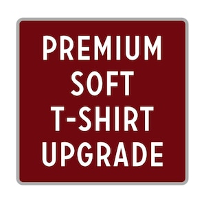 May include: A burgundy square sign with rounded corners and a white border. The sign says "PREMIUM SOFT T-SHIRT UPGRADE" in white text.
