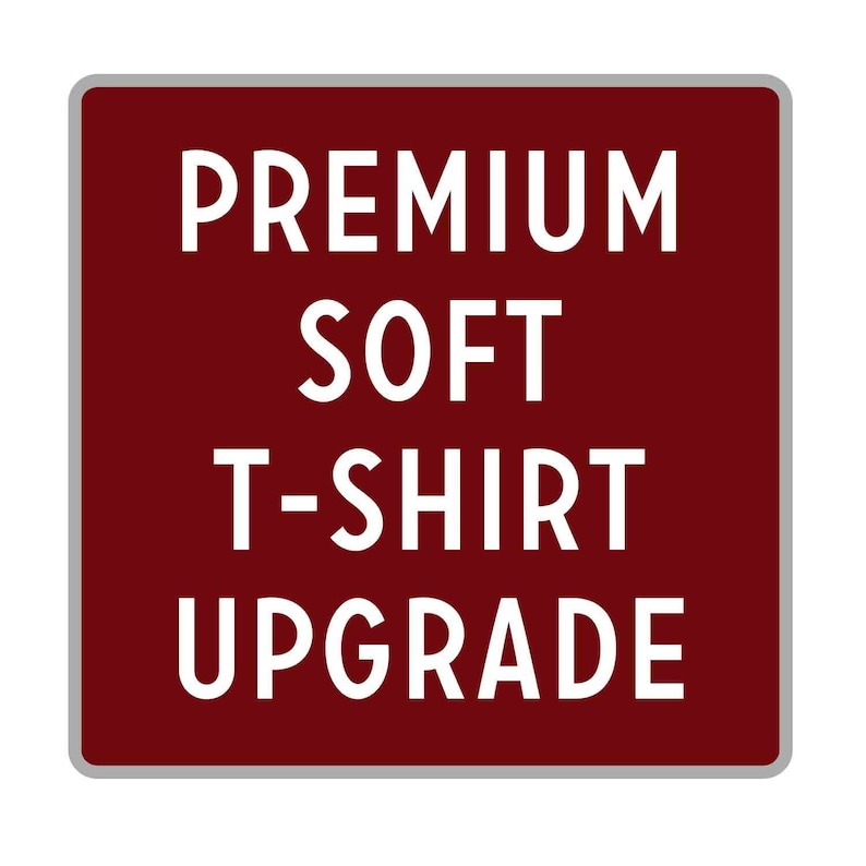 May include: A burgundy square sign with rounded corners and a white border. The sign says "PREMIUM SOFT T-SHIRT UPGRADE" in white text.
